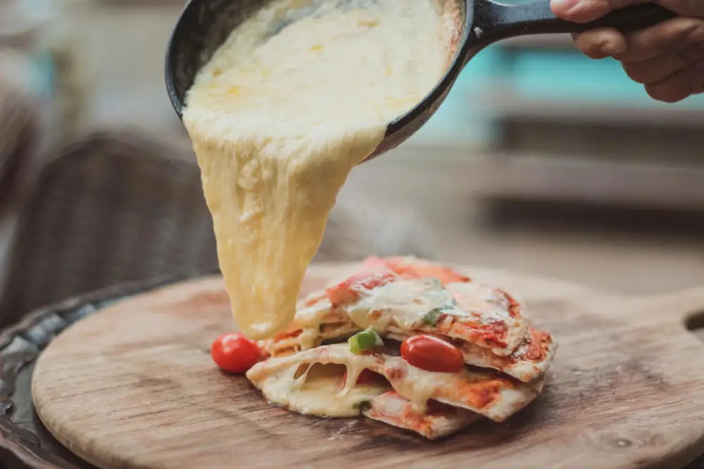 pouring melted cheese on pizza from the pan