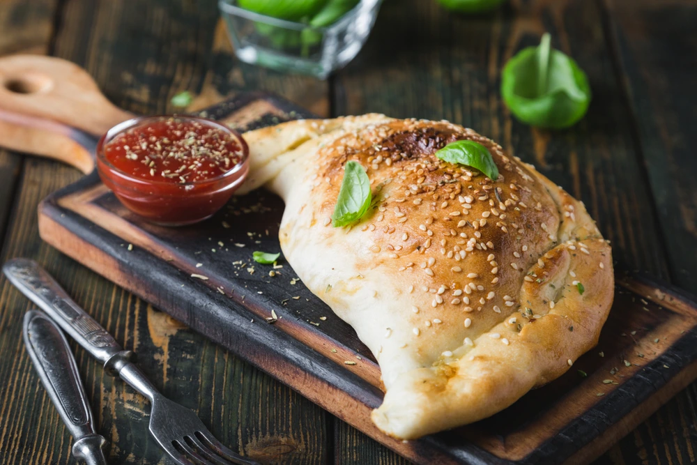calzone kept on a wooden board with sauce